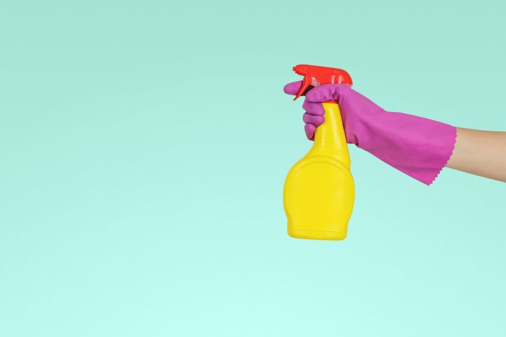 Persoon houd een schonnmaak fles vast met een rubberen handschoen voor schoonmaken 