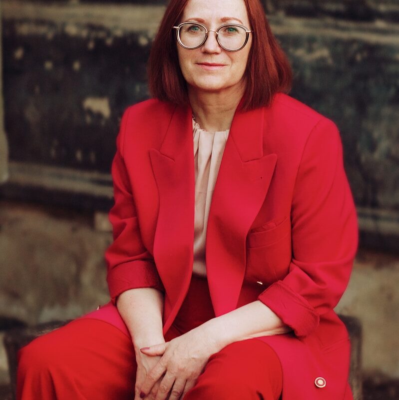 a woman in a red suit sitting on a tree stump