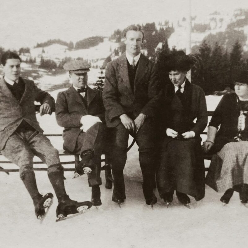 A vintage photo of a family group ice skating outdoors in winter.