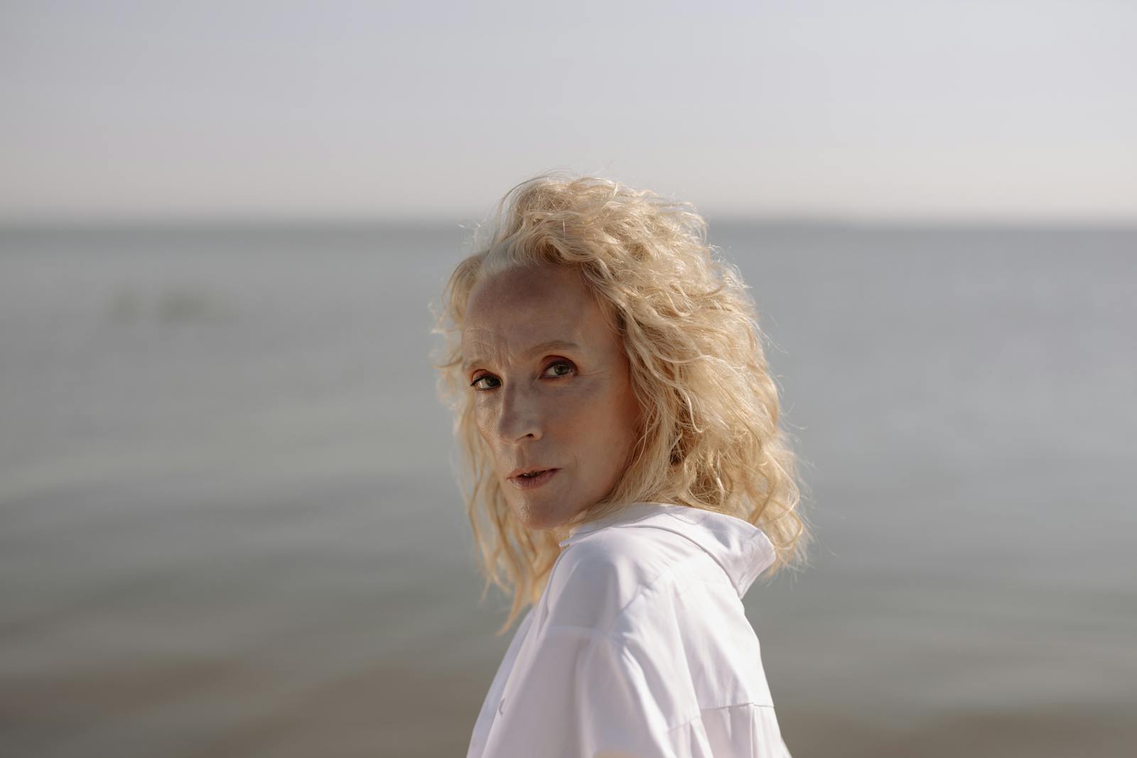 Stylish senior woman poses gracefully at the beach, exuding elegance and poise.